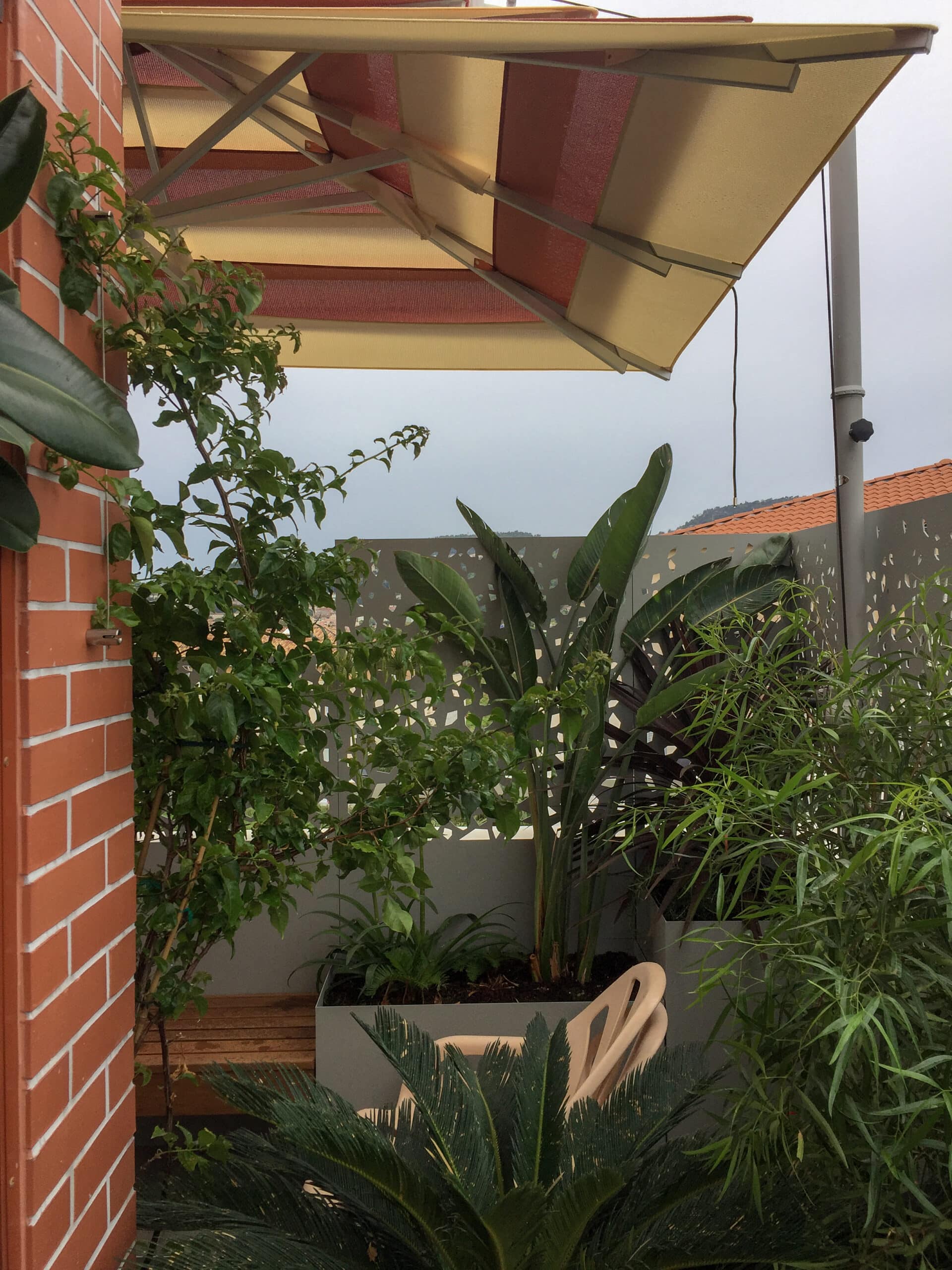 Terrasse urbaine avec plantes exotiques, store rayé jaune et mur en briques rouges créant un jardin de balcon privé.