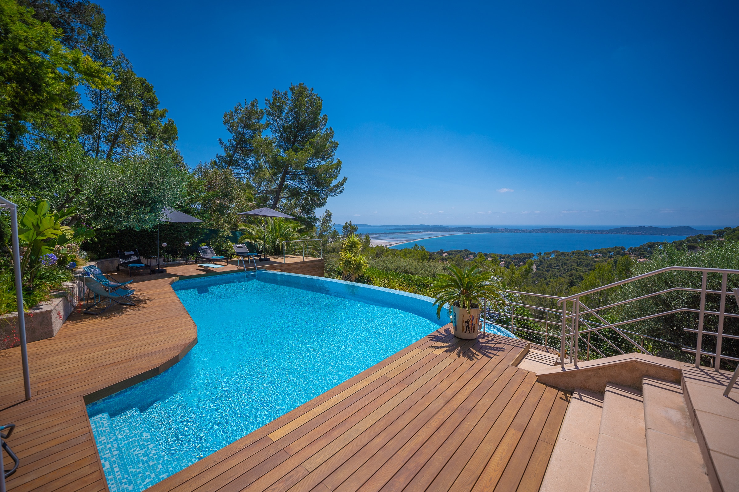 Piscine à débordement et terrasse en bois avec vue panoramique sur la mer Méditerranée et la côte sauvage.