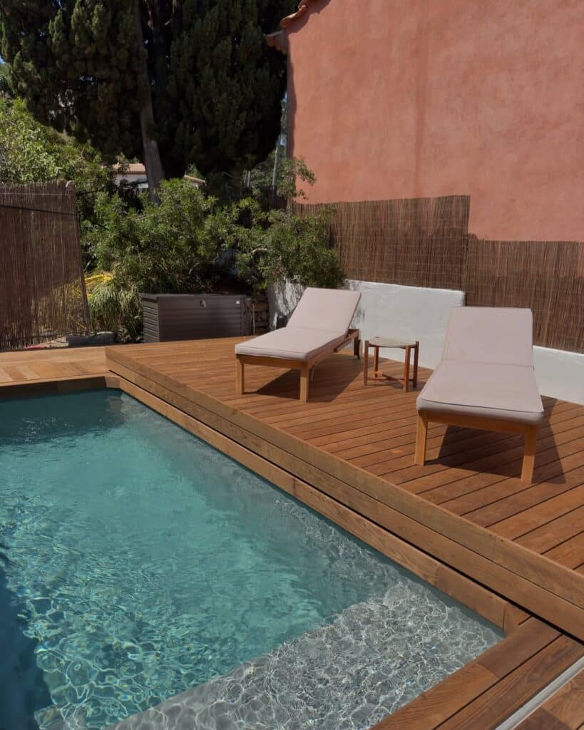 Terrasse en bois avec piscine et transats de jardin Terrasse en bois avec transats au bord d'une piscine bleue devant un mur ocre ensoleillé.