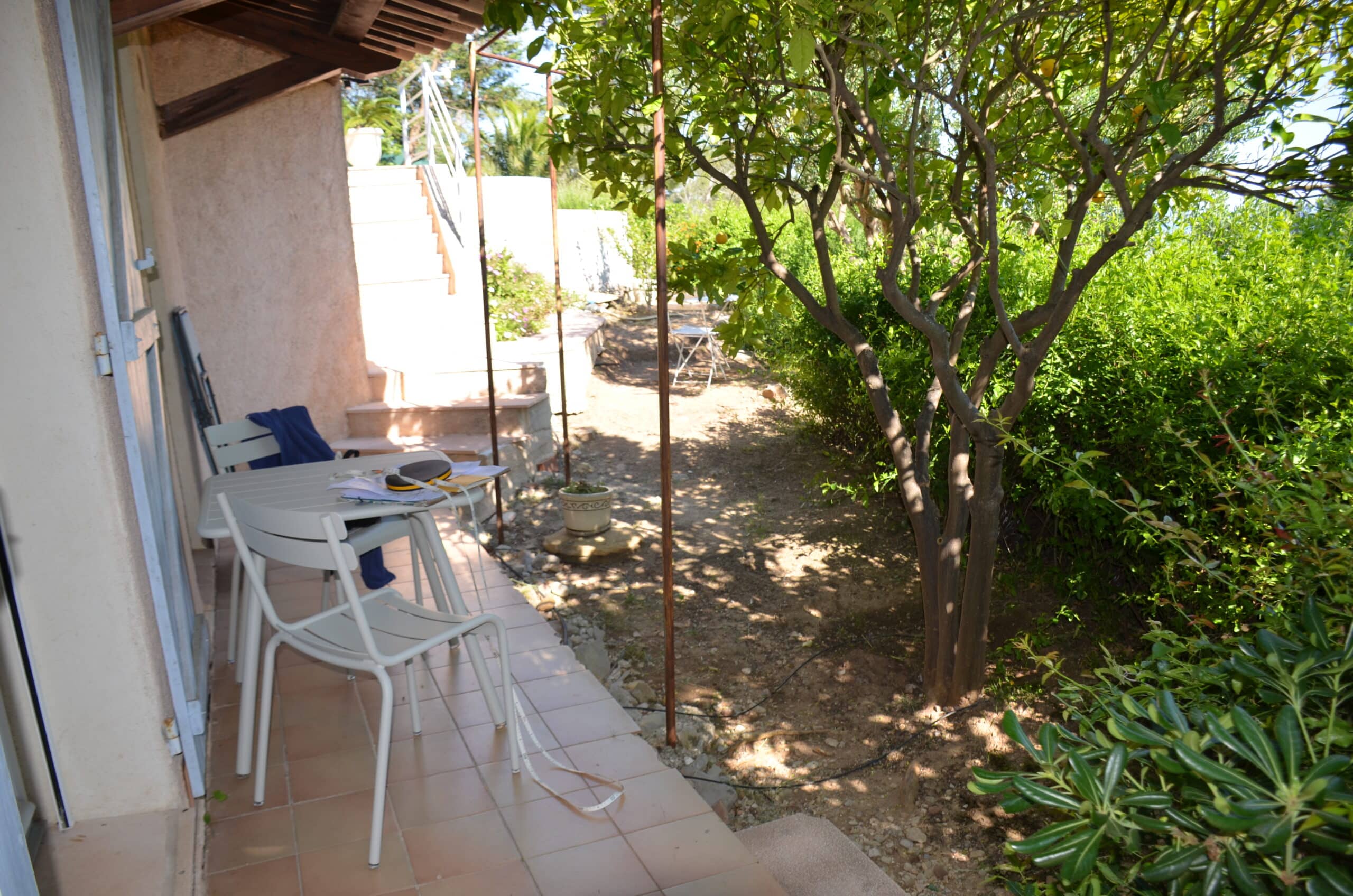 Table de terrasse avec mètre ruban devant un citronnier ensoleillé dans un jardin méditerranéen.