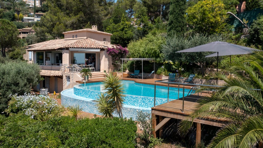 Villa avec Piscine à Débordement et Terrasse de Luxe Villa provençale avec piscine à débordement à plusieurs niveaux, terrasse en bois et jardin méditerranéen ensoleillé.
