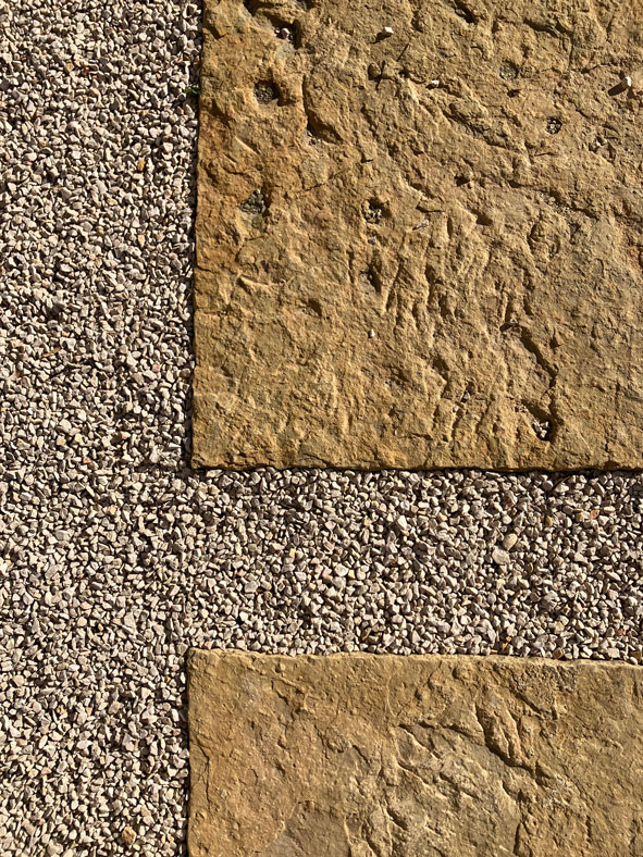 Dalles de pierre jaune texturées entourées de petits graviers clairs pour un aménagement paysager de jardin.