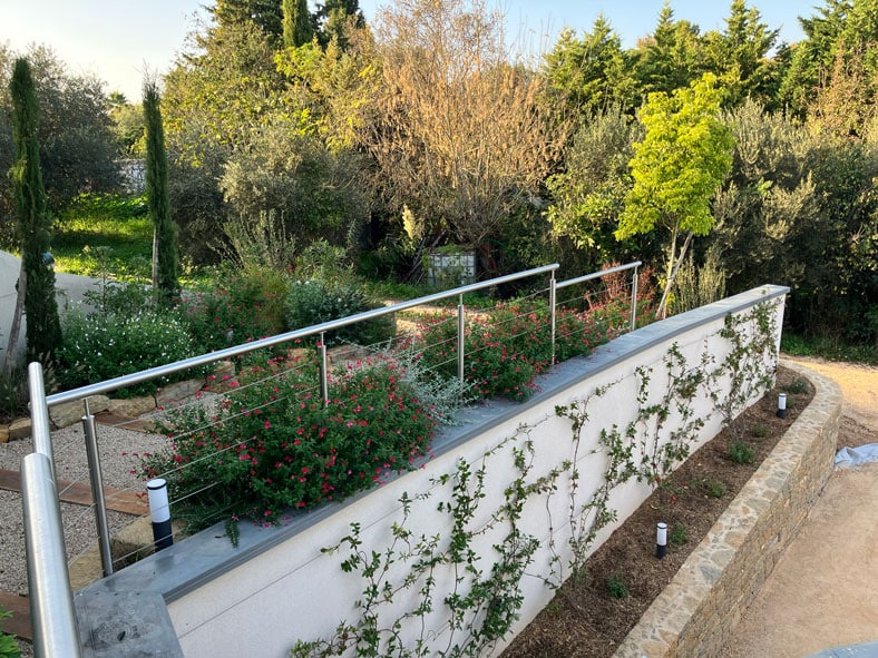 Garde-corps inox et fleurs rouges sur un mur blanc végétalisé dans un jardin paysager moderne.