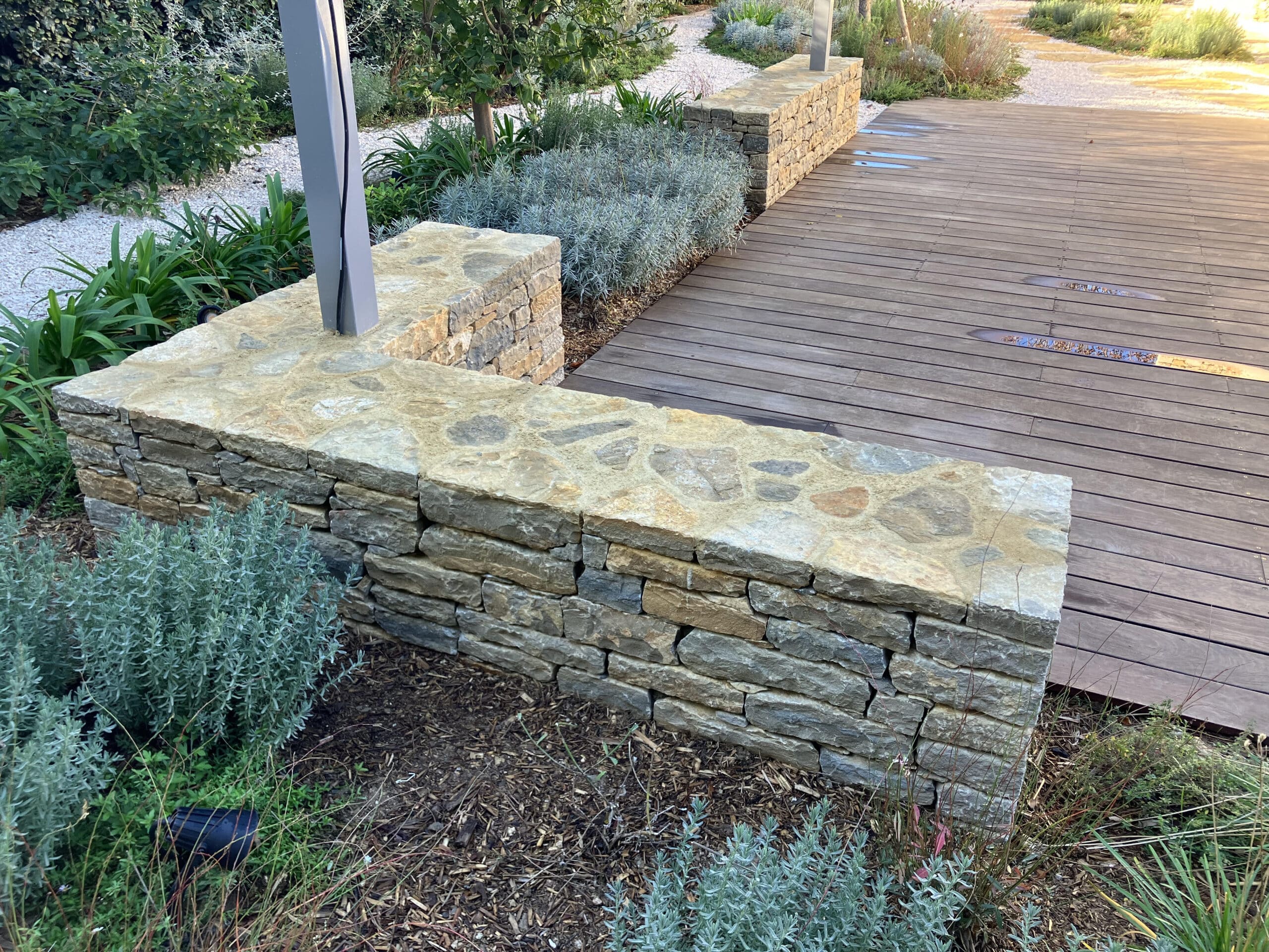 Mur en pierre naturelle et terrasse en bois dans un jardin paysager avec lavande et paillis.