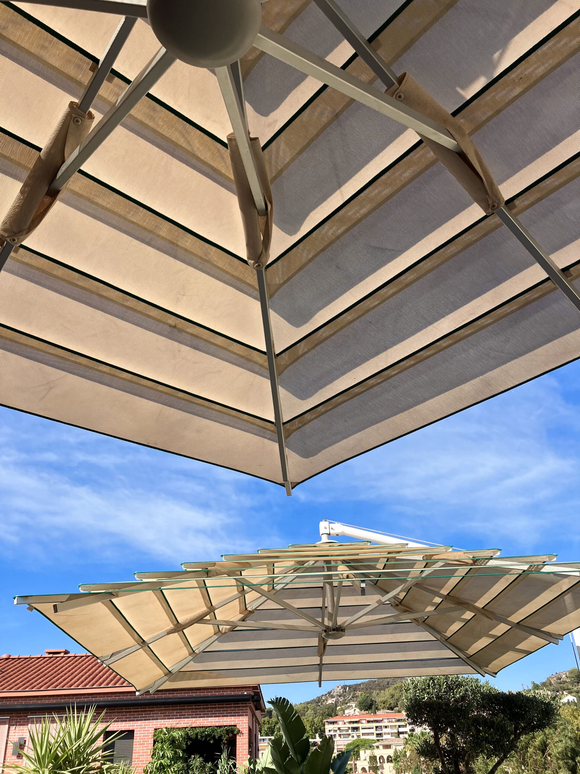 Deux parasols de terrasse rayés vus d'en bas sous un ciel bleu dégagé lors d'une journée ensoleillée.