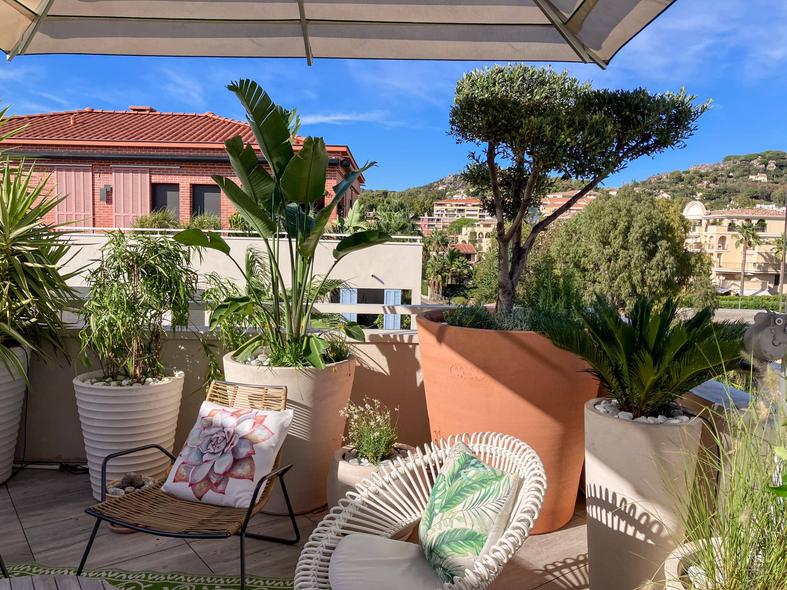 Balcon avec oiseau de paradis, olivier RAVEL FRANCE et fauteuils design sous un parasol face aux collines.