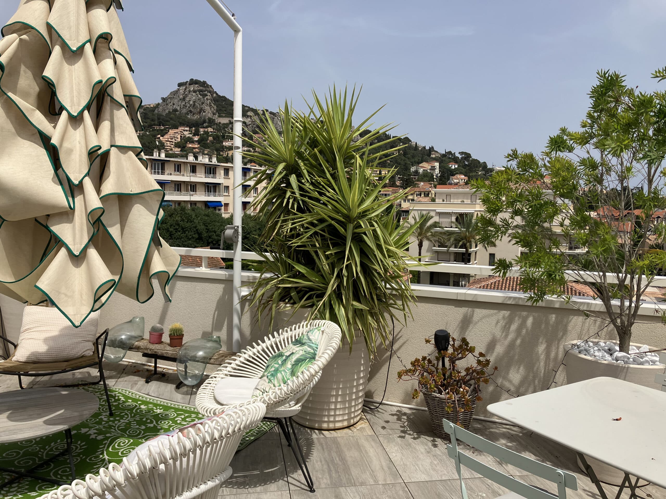 Terrasse de toit aménagée avec fauteuils blancs, plantes vertes et vue sur une colline escarpée.